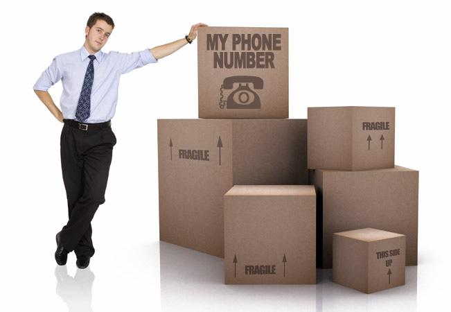 Man wearing a suit leaning against cardboard boxes that say 'My Phone Number' on the boxes.